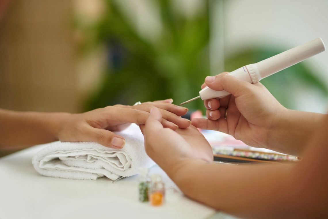 Person receiving professional manicure with hands gently held and nails being polished. Manicurist's tools and supplies visible on table